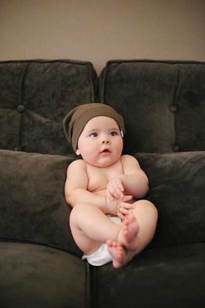 A baby sitting propped up on a sofa wearing a diaper