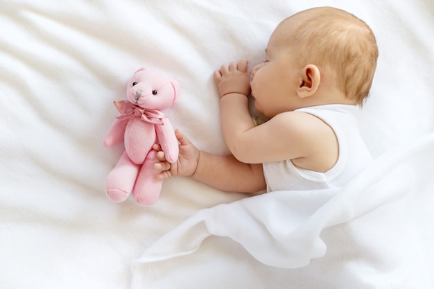 Baby slaapt met een teddybeer op een witte achtergrond.