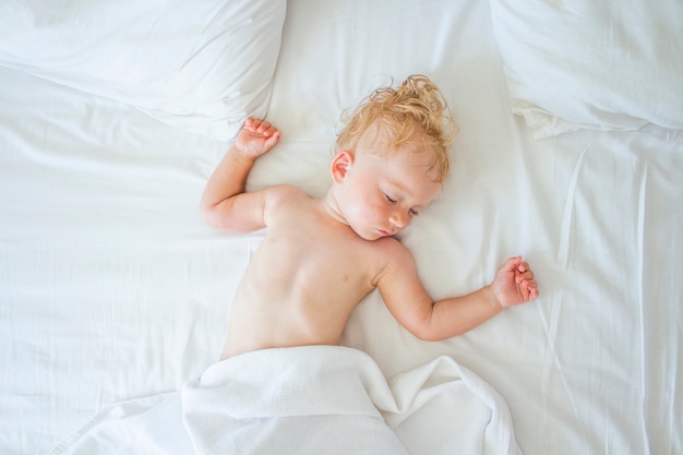 Baby sleeps in bed with white sheets. The concept of a good and sound baby sleep. Flat lay, top view. Copy space