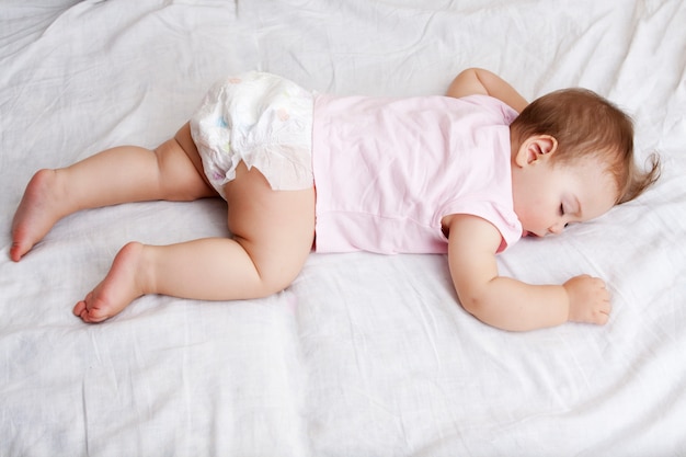 The baby sleeps on his stomach on a white bed