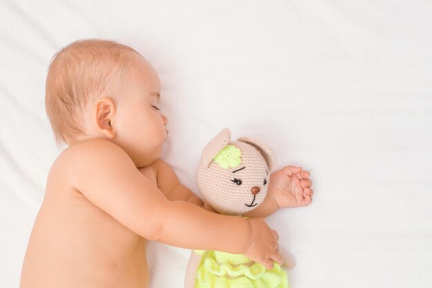 Baby sleeps hugging his favorite knitted toy, copy space