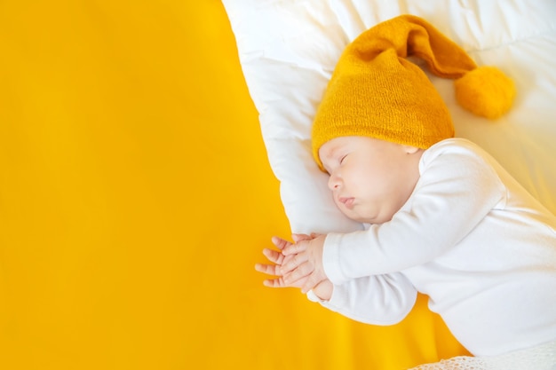 Baby sleeps with hat on a yellow background, winter and holiday concept