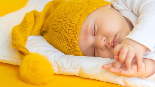 赤ちゃんは黄色の背景、冬と休日の概念の帽子で眠る