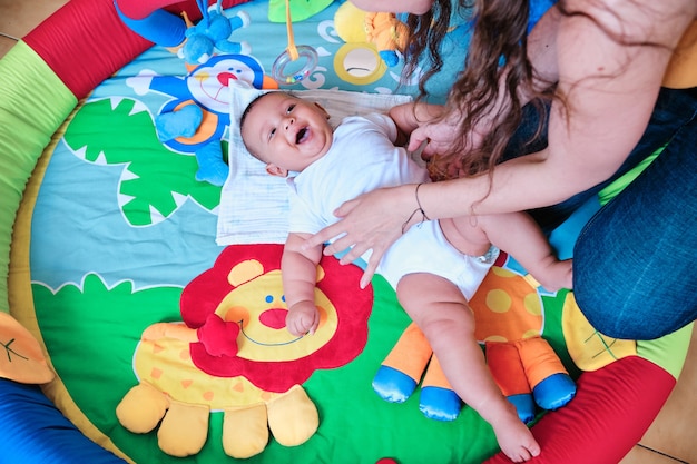 Baby smiling while playing with his mother on the floor at home.