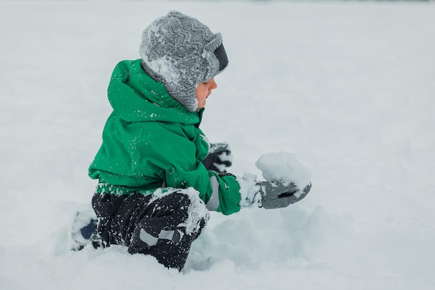 Baby speelt in de sneeuw sneeuwspelletjes in de frisse lucht babyplezier baby39s spel een sneeuwpop beeldhouwen