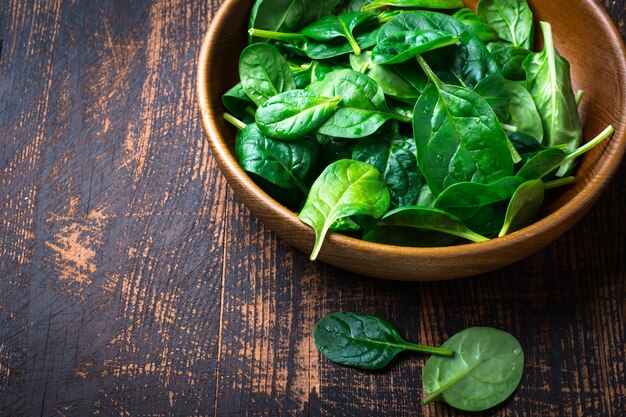 Baby spinach leaves in a bowl on dark background.