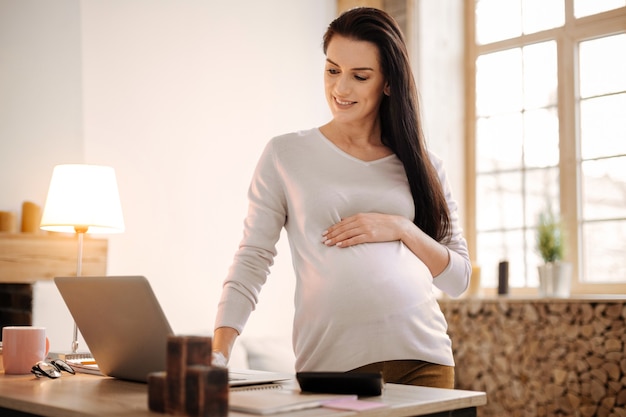 Детские вещи. Очаровательная оптимистичная беременная женщина обнимает Тимми, глядя на экран и оставаясь