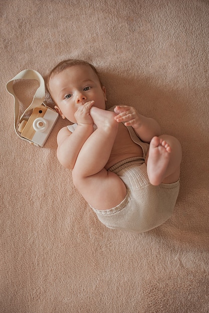 Foto il bambino succhia le dita dei piedi su uno sfondo beige