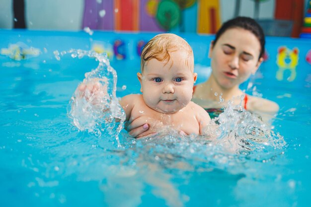 Фото Ребёнок, плавающий в бассейне, учит новорожденного мальчика плавать в басейне с тренером.