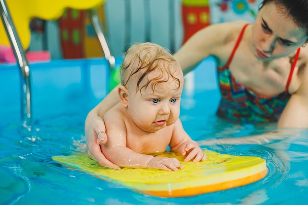 Baby swimming in the pool teaching a newborn boy to swim in a pool with a coach