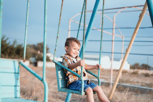 Baby on swing swinging one near the sea, in shirt and denim shorts