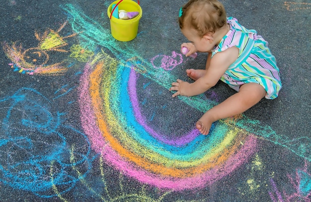 Baby tekent een regenboog op de stoep met krijt. Selectieve aandacht. Natuur.