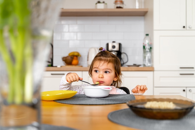 Baby toddler girl eats soup with spoon in her hand.