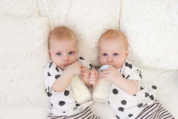 Baby-tweelingen liggen in hun pyjama op het bed en drinken melk uit flessen