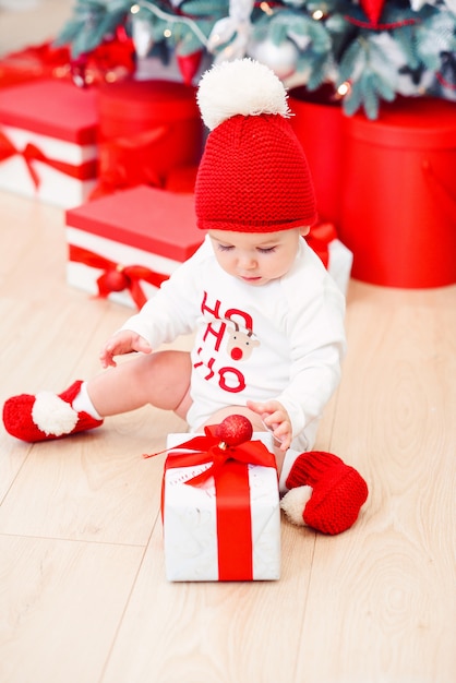 아기 산타, bokeh 빛, 겨울 휴가 개념으로 옷을 입고 크리스마스 장식 선물 상자를 풀고