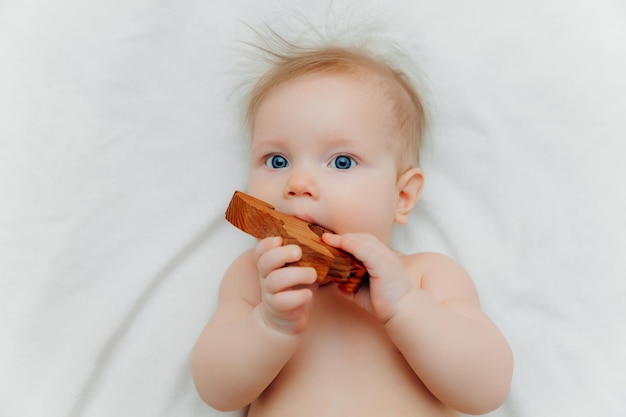 Baby van 6 maanden oud houdt in zijn handen een houten bijtspeeltje liggend in een wieg in een kinderkamer
