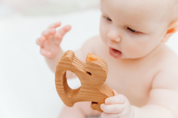 Baby van 6 maanden oud houdt in zijn handen een houten bijtspeeltje liggend in een wieg in een kinderkamer