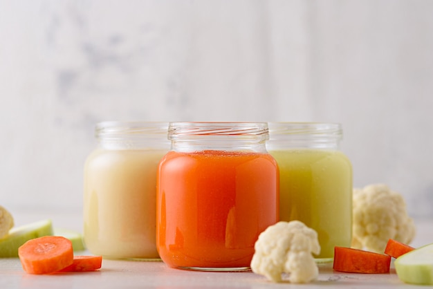 Baby vegetable puree of carrots, zucchini, cauliflower in glass jars on white