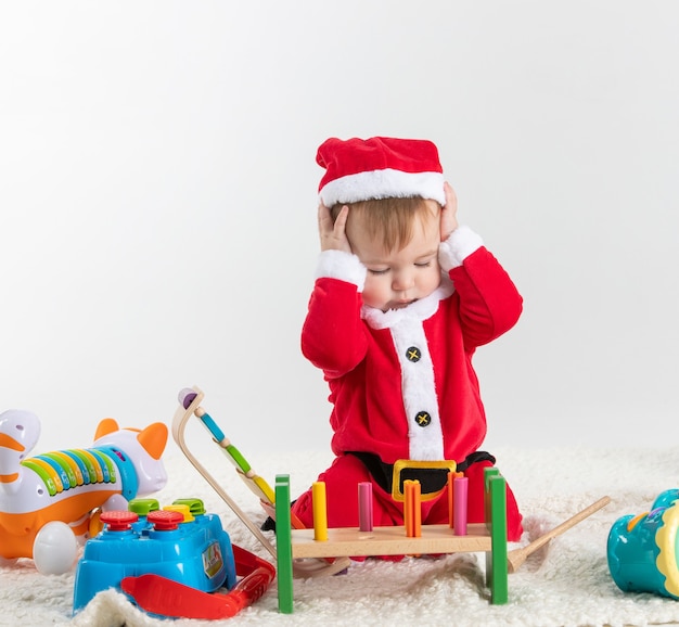 Baby verkleed als kerstman zittend op de vloer spelen met houten en plastic speelgoed.