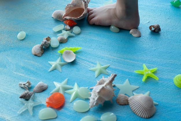 Foto baby voeten op schelpen zomer achtergrond veel verschillende zeeschelpen zeester op een achtergrond van blauwe verfstreken plaats voor tekst