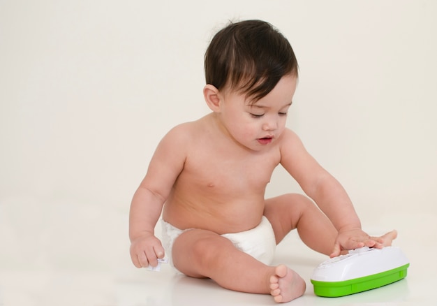 Baby wears white disposal diaper is playing with toy