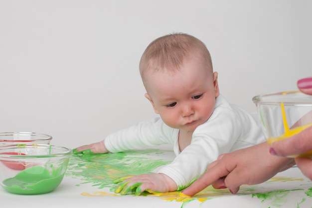 Baby on a white background in a white pajamas with paints