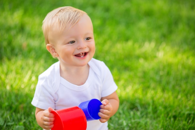 Bambino in un body bianco seduto sull'erba verde giocando