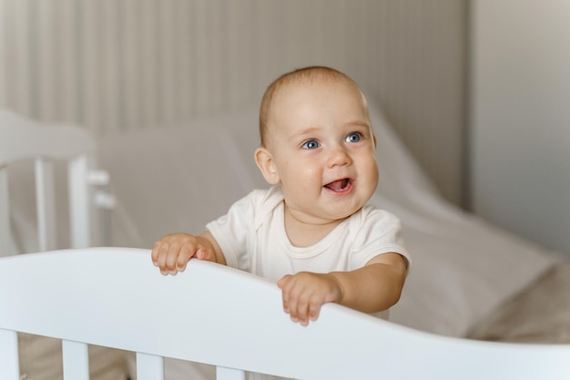 Baby in a white bodysuit in a white crib large portrait, smiling