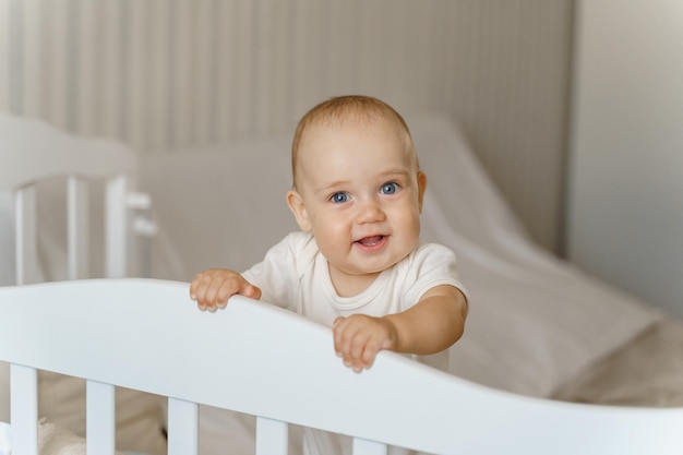 Baby in a white bodysuit in a white crib large portrait, smiling