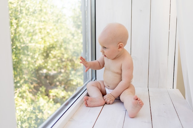 Baby on the window in diapers at home