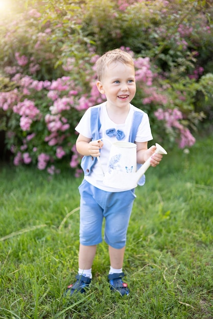 Baby with blue eyes in summer a sunny day the child laughs holds a watering can waters flowers