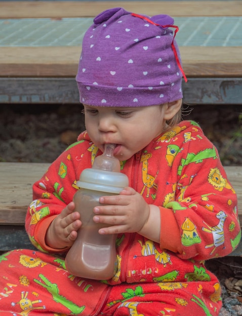 A baby with a bottle food on a cloudy day.