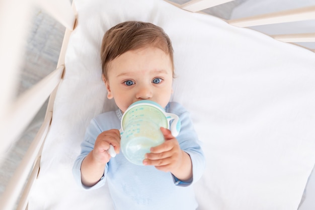 Baby with a bottle of milk in his hands in the crib eating, baby food concept