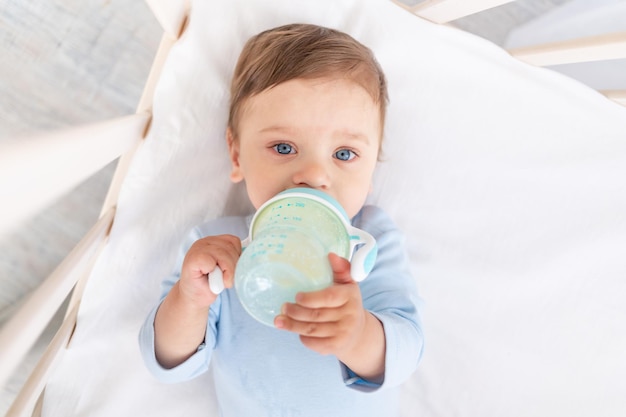 Baby with a bottle of milk in his hands in the crib eating baby food concept