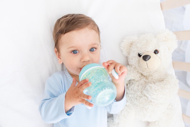 Baby with a bottle of milk in his hands in the crib eating baby food concept