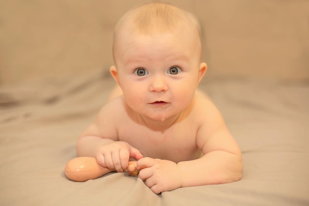 A baby with a brown egg on its face is laying on a beige blanket.