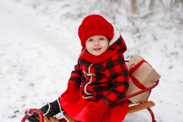 Baby with expressive eyes in red coat is sitting on sled