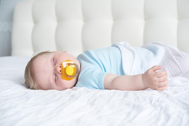 Photo a baby with a pacifier in his mouth is sleeping on the bed