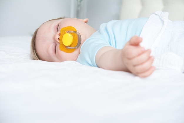 Photo a baby with a pacifier in his mouth is sleeping on the bed