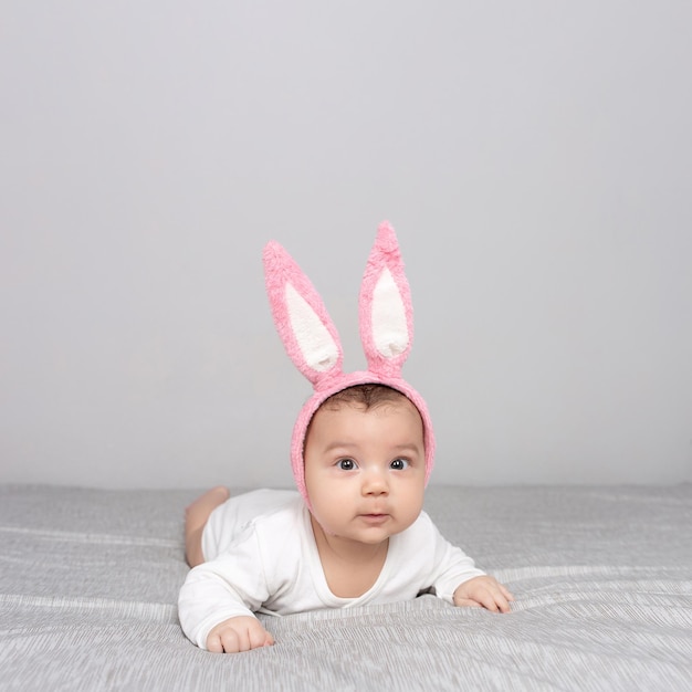 Baby with rabbit ears lies on a gray light bed The concept of a Happy Easter Mockup for advertising design celebration postcards Copy space