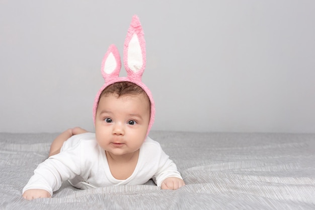 토끼 귀를 가진 아기는 회색 빛 침대에 놓여 있습니다. 광고 디자인 축하 엽서 공간을 복사하기 위한 행복한 부활절 모형의 개념