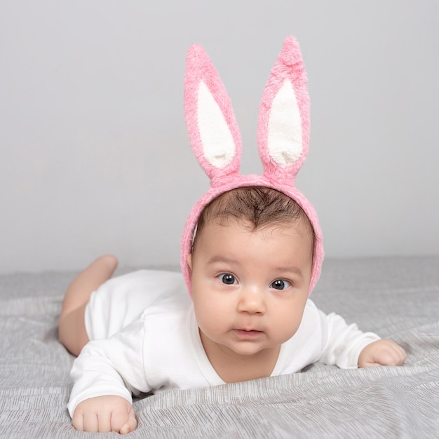 Baby with rabbit ears lies on a gray light bed The concept of a Happy Easter Mockup for advertising design celebration postcards Copy space