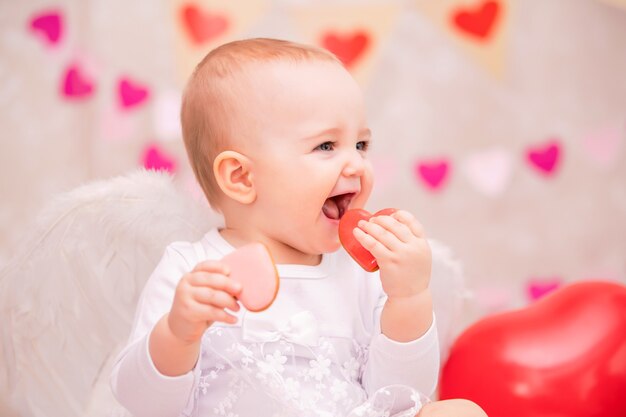 Baby with white feather wings eats heart-shaped cookies