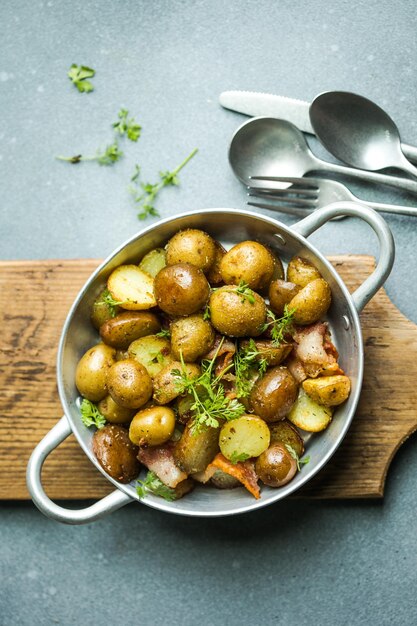 Baby young potatoes bacon parsley on a frying pan on a wooden background closeup