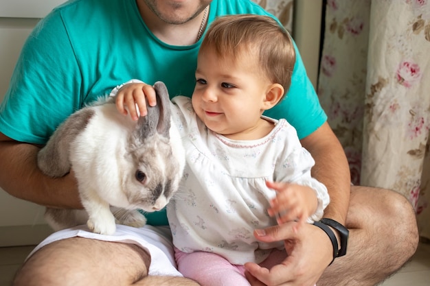 Baby zit in vaders armen en aait een decoratief konijn als huisdieren in een gezin met kinderen