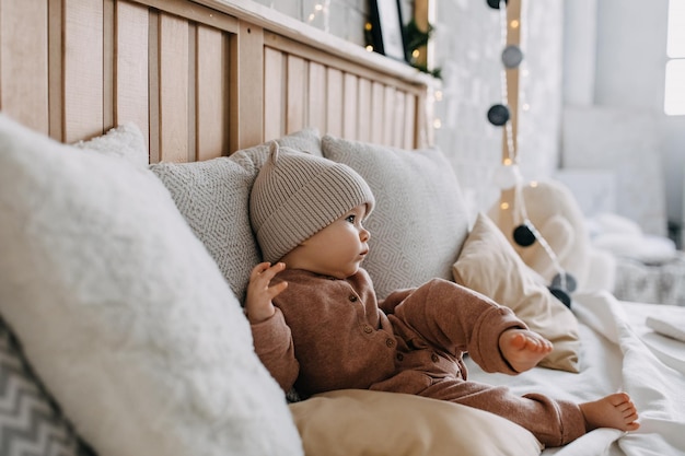 Baby zittend op bed tussen kussens thuis met een muts met oren