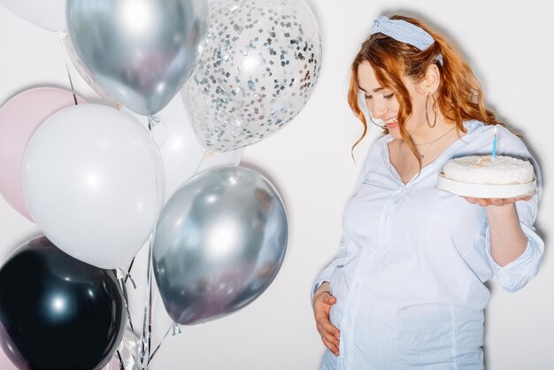 Babyboom gelukkige vrouw genieten van zwangerschap feestelijke partij mooie momenten vrolijke buik dame bedrijf taart kaarslicht teder aanraken buik geïsoleerd witte kleurrijke ballonnen decoratie