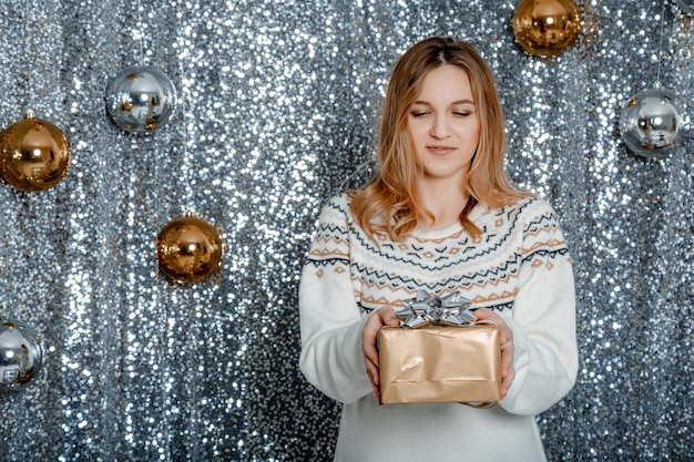 Babydouche-concept. Gelukkig Zwangere Dame Bedrijf Verpakt Geschenkdoos Kijken Camera Staande. Buik van een zwangere vrouw met een kerstspeelgoed in haar handen.