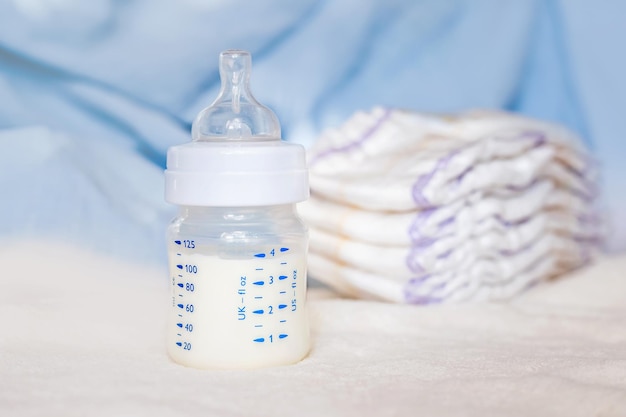 Babyfles met melk en luiers op een witte stoffen achtergrond babyverzorging eerste dagen van het leven voeding en moederschap