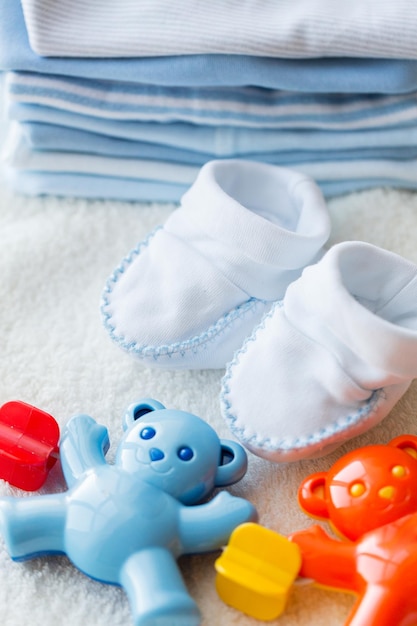 детство, детство, игрушки, одежда и концепция объекта - крупный план детской погремушки с пинетками и одежда для новорожденного мальчика на полотенце
